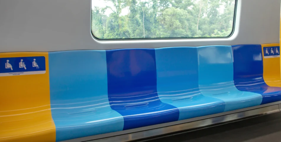 Empty blue and yellow plastic train seats are shown beneath a window with a view of green trees outside. Signs indicate reserved seating areas.