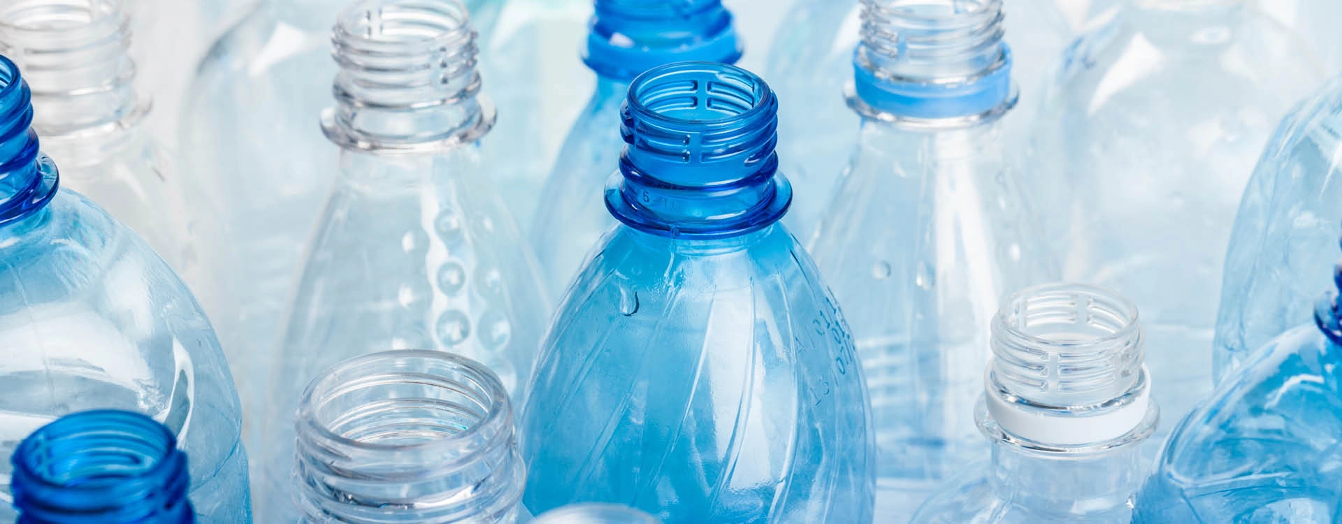 A collection of empty, clear and blue plastic bottles with their caps removed, arranged closely together.