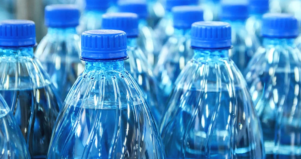 Rows of clear plastic water bottles with blue caps are shown closely packed together.