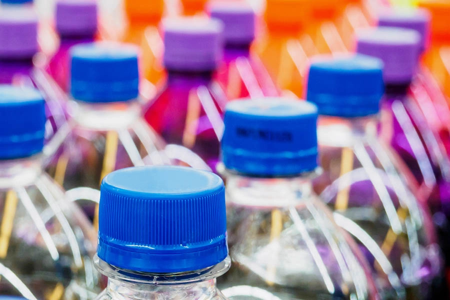 Close-up of several plastic bottles with blue and purple caps, arranged in rows, with colorful liquid contents visible.