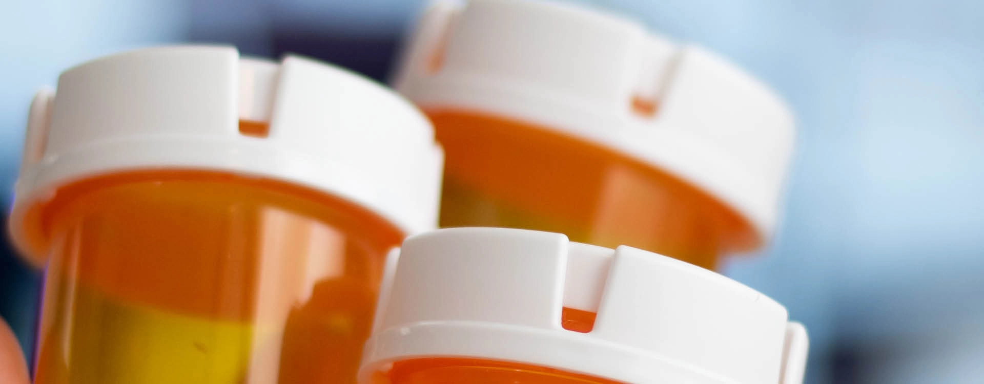 Close-up of three orange prescription pill bottles with white child-proof caps against a blurred blue background.