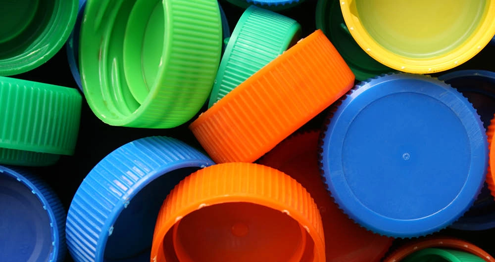 A close-up view of assorted colorful plastic bottle caps, including green, blue, orange, and yellow caps, stacked and overlapping each other.