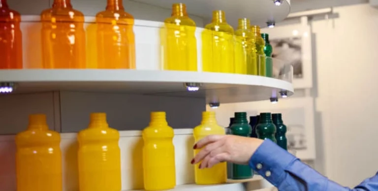 A person arranges colorful bottles in shades of orange, yellow, and green on curved white shelves.