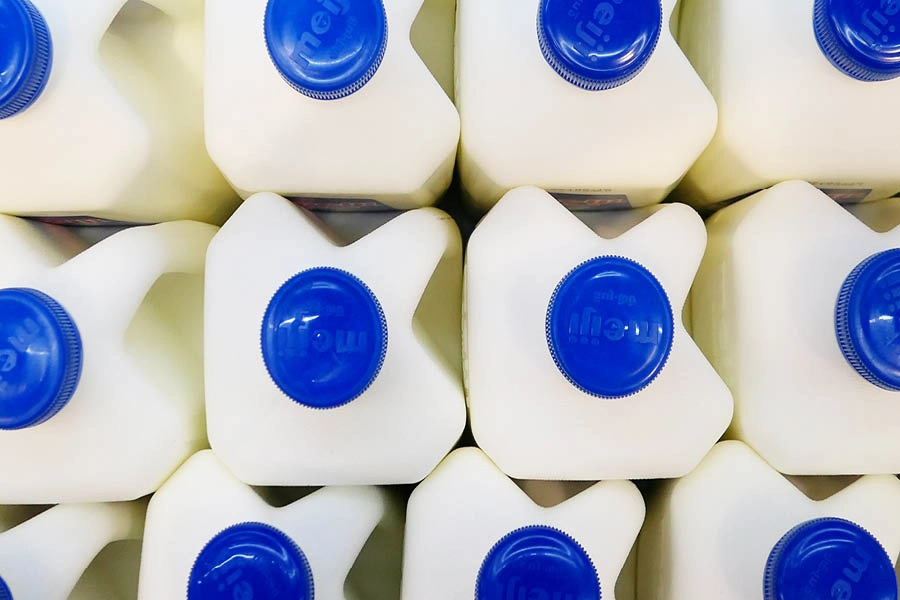 A top-down view of several white plastic milk jugs with blue caps arranged in a neat, grid-like pattern.