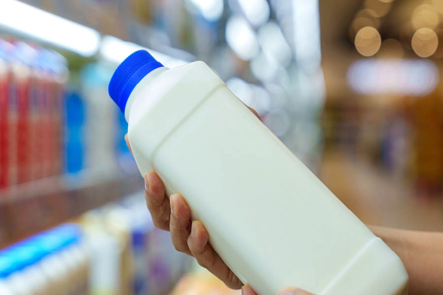 A person holds a white plastic bottle with a blue cap in a grocery store dairy aisle.