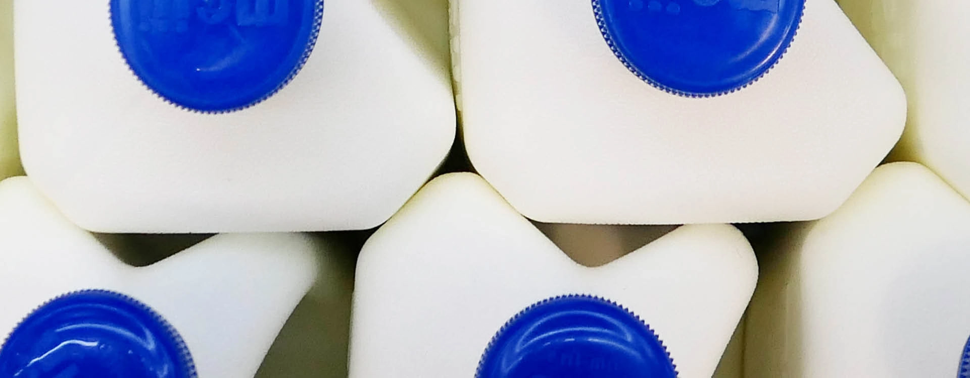 Close-up view of stacked white plastic milk jugs with blue caps, arranged so that only the tops and caps are visible.
