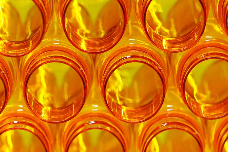 Close-up view of multiple empty orange plastic bottles arranged in rows, seen from above with light shining through them.