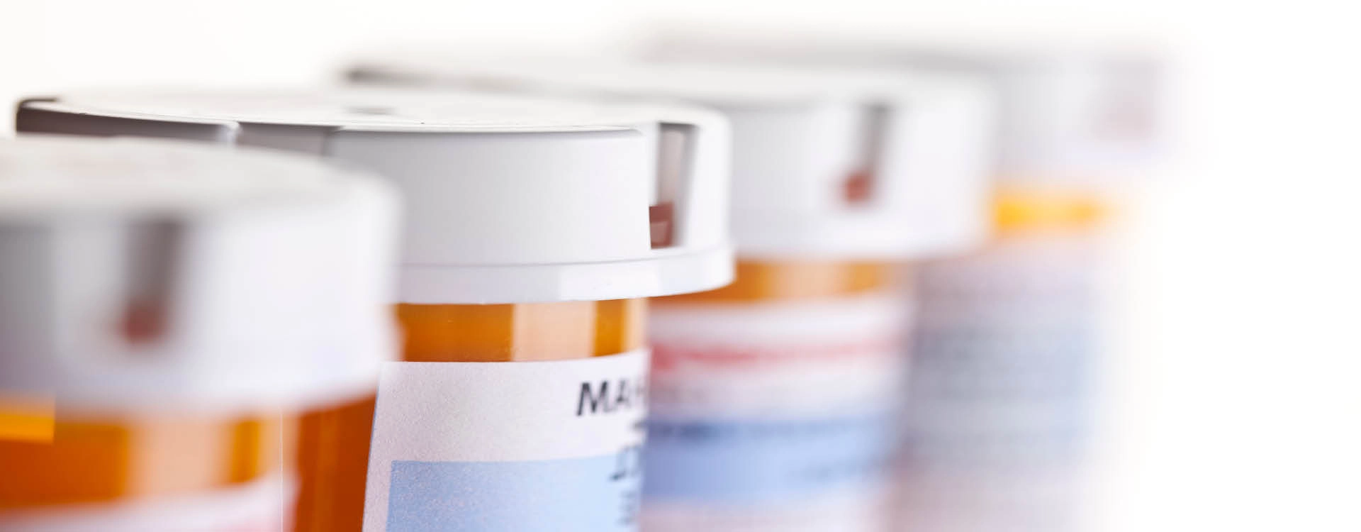 Four prescription pill bottles with white caps are lined up in a row, labels partially visible, against a white background.