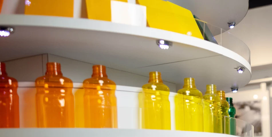 Shelves displaying transparent plastic bottles in shades of orange, yellow, and green, with yellow rectangular objects on the upper shelf.