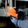 A person wearing gloves holds two orange plastic pieces with attached runners, likely parts just removed from an Americhem injection molding process.