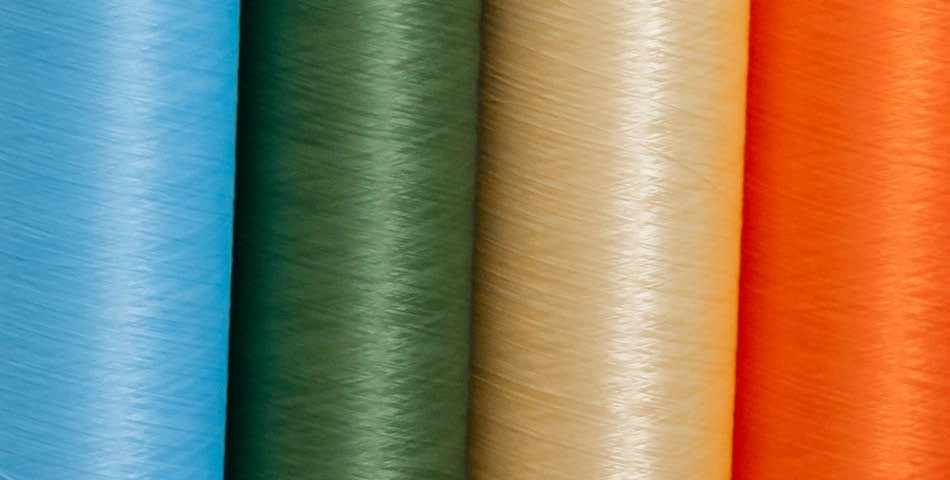 Close-up of five vertical spools of thread in blue, green, beige, yellow, and orange colors.