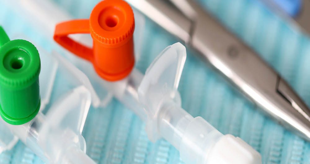 Close-up of medical devices including syringes with green and orange caps and metal scissors, placed on a blue textured surface.