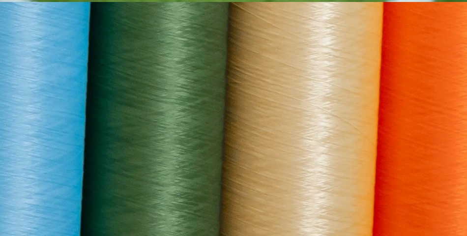 Close-up of five large spools of thread in blue, green, beige, yellow, and orange, arranged side by side in vertical orientation.