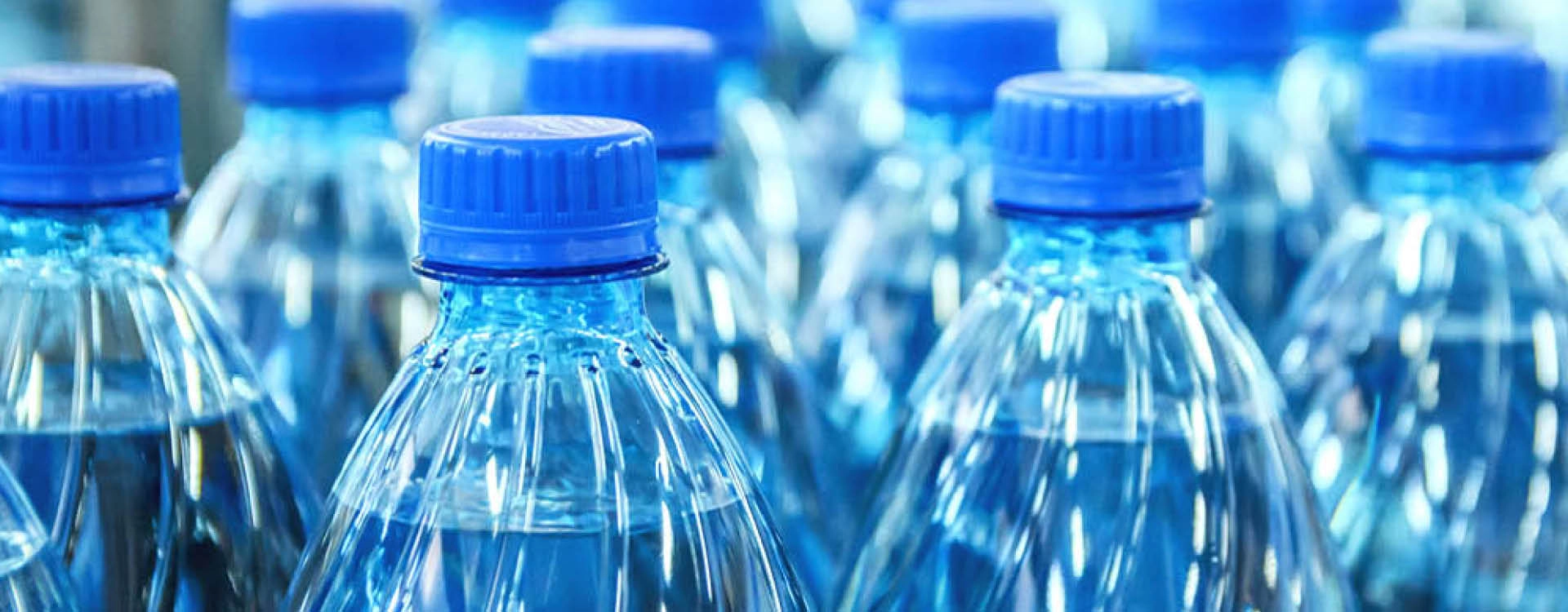 Close-up view of several plastic water bottles with blue caps, filled with clear water and grouped together in rows.