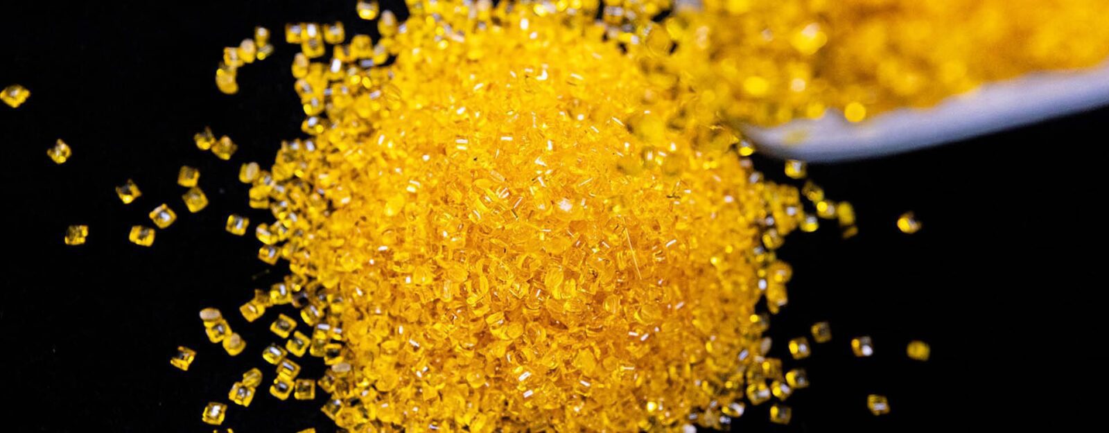A pile of small, yellow, translucent plastic pellets is scattered on a black surface.