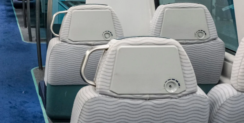 Rows of gray patterned seats inside a vehicle, each with a headrest, a circular vent, and a metal handle.