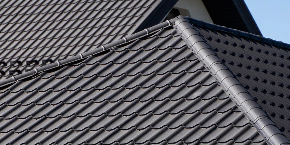 Close-up view of multiple intersecting rooftops covered with dark gray, wavy roof tiles, showing clean lines and a uniform pattern.