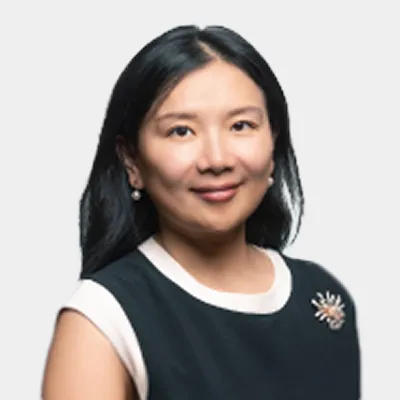 Woman with long black hair wearing a sleeveless black top with white trim and a decorative brooch, smiling at the camera against a plain light background.