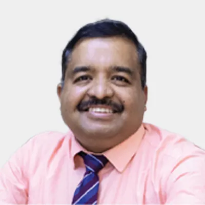 Man with short dark hair and a moustache, wearing a light pink shirt and striped tie, smiling at the camera against a plain background.