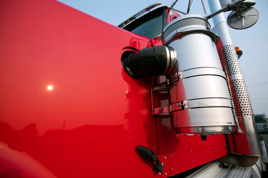 Close-up view of the side of a red semi truck, showing part of the hood, an air filter, and a side mirror against a clear sky.