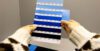 A person holds a color swatch card displaying multiple shades of blue, each labeled with codes, against a plain background.