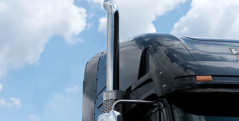 Close-up of the top front section of a black semi-truck cab with a vertical exhaust pipe, against a blue sky with scattered clouds.