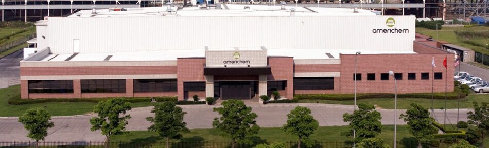 A large industrial building labeled "Americhem" with a brick facade, surrounded by greenery and a parking lot with several cars.