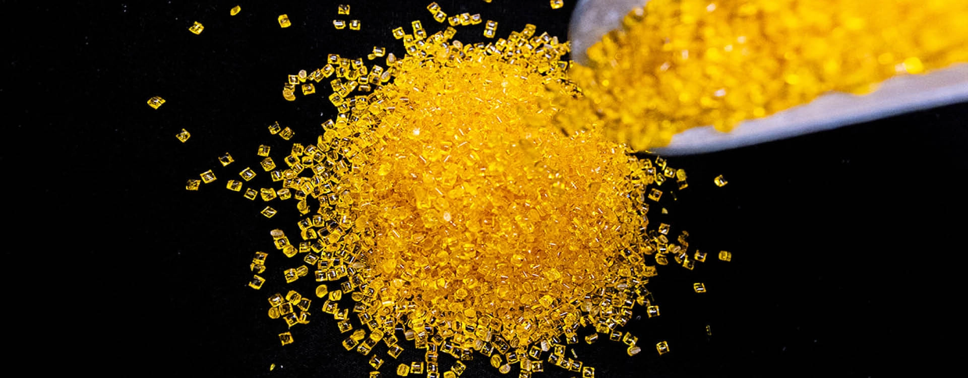 A pile of small yellow plastic pellets is being poured from a container onto a black surface.
