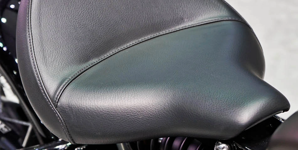 Close-up view of a black leather motorcycle seat, showing its smooth texture and stitching details.
