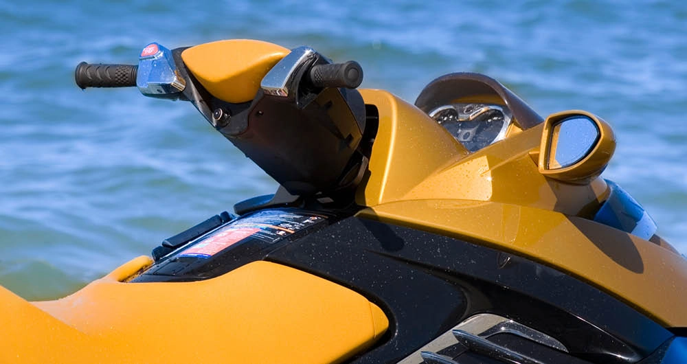 Close-up of the handlebars and dashboard of a yellow personal watercraft, with the ocean visible in the background.