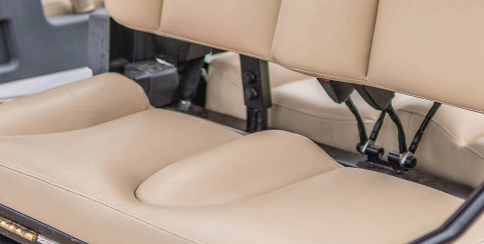 Close-up view of a beige, cushioned seat with two seat belts in the back of a vehicle, possibly a golf cart or utility vehicle.