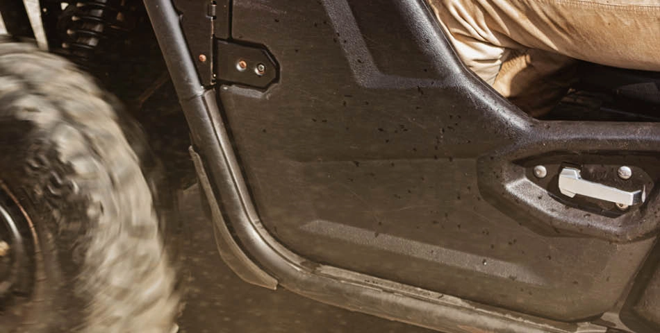 Close-up of the side of an off-road vehicle, showing a large tire, a metal door, and part of a person wearing light-colored pants.