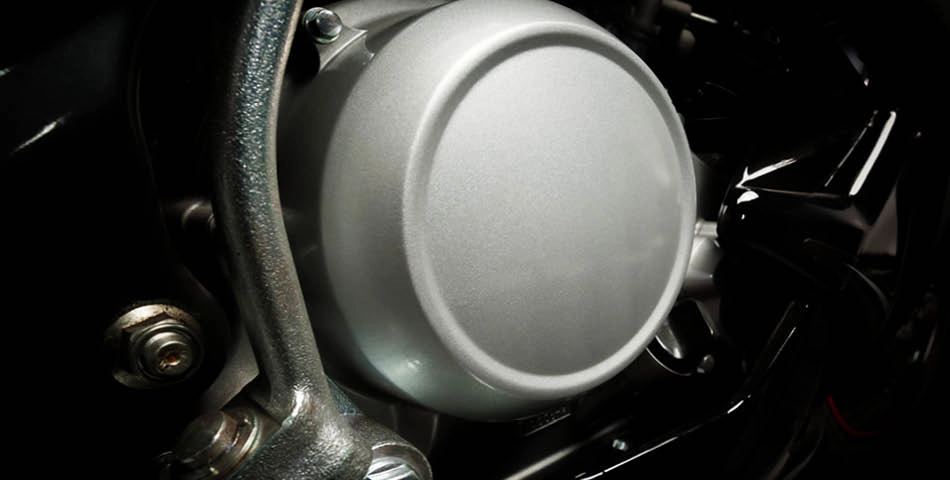 Close-up view of a metallic motorcycle engine cover with bolts and surrounding components visible.