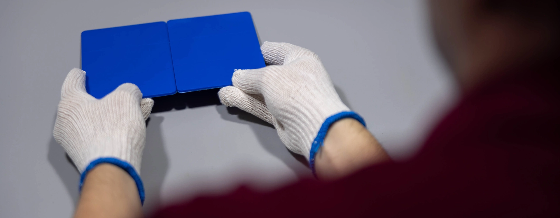 A person wearing white gloves is holding and aligning two blue rectangular panels on a flat gray surface.