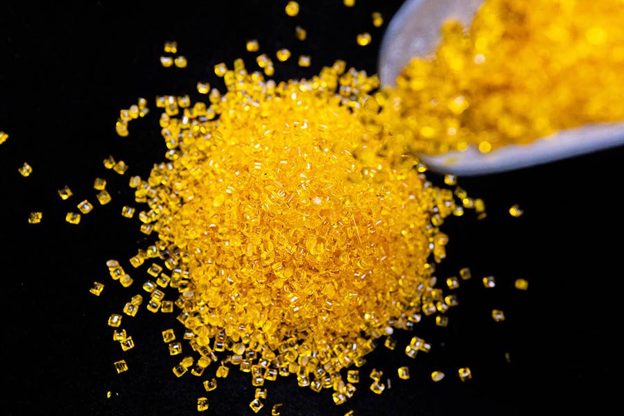 A pile of small, yellow, translucent plastic pellets is shown on a black background, with some being poured from a container.
