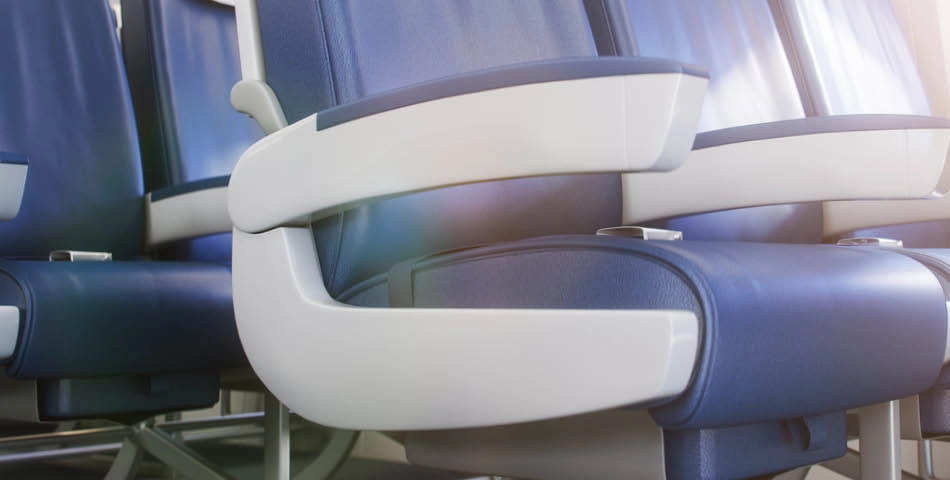 Close-up view of blue and white airplane seats with armrests, showing details of the upholstery and design. Sunlight is visible on the seats.