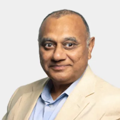 A middle-aged man with short hair wearing a beige blazer and light blue shirt, posing for a professional headshot against a plain light background.