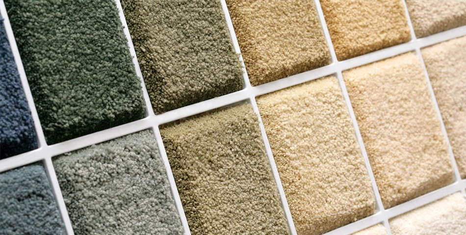 Close-up of carpet sample squares in various shades of green, beige, and tan arranged in a grid pattern.