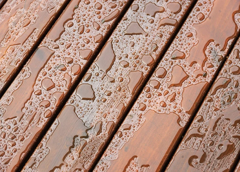 Close-up of water droplets on wooden planks, showing moisture patterns on the reddish-brown surface.