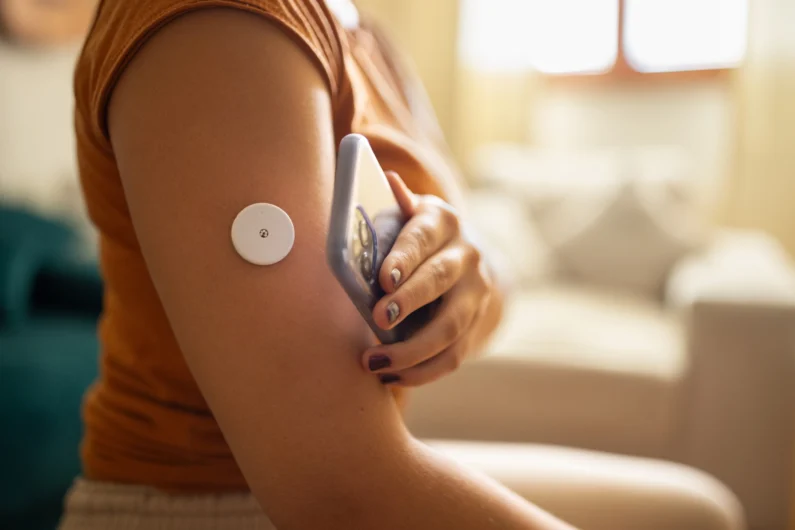 Close-up of a person scanning a sensor on their upper arm with a smartphone, likely monitoring glucose levels or health data at home.