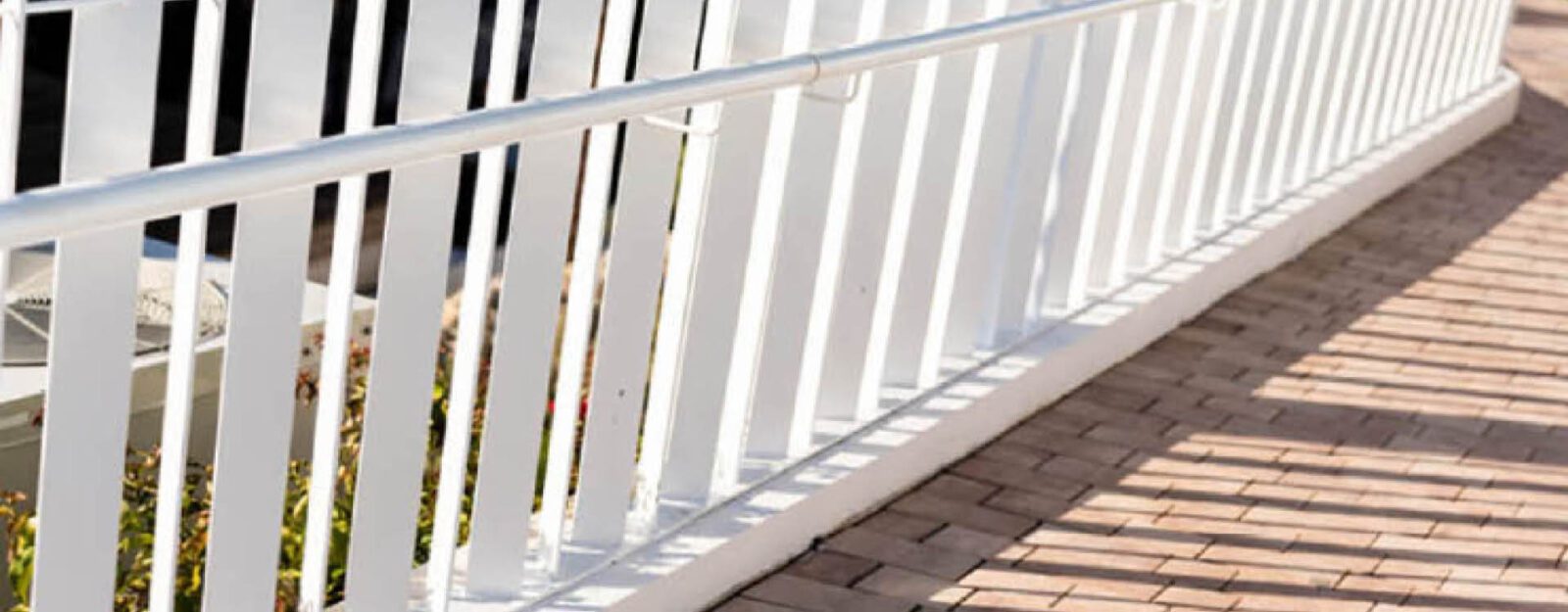 A white metal handrail runs alongside a sloped brick pathway, providing support and accessibility.