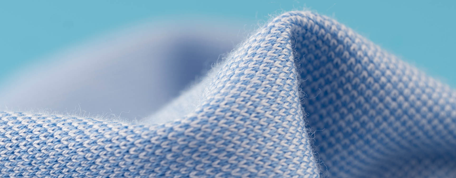 Close-up of light blue textured fabric with a visible knit pattern, slightly folded against a soft blue background.