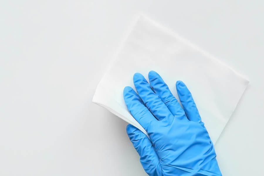 A hand wearing a blue glove wipes a white surface with a white cloth.