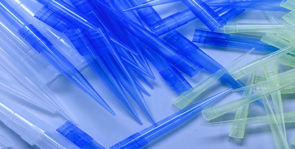 A pile of assorted blue, clear, and yellow plastic pipette tips—made from durable, chemical-resistant, and recyclable polyolefin compounds—scattered on a light surface.
