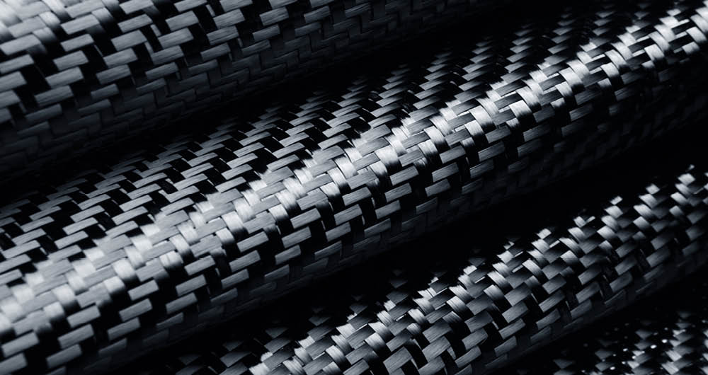 Close-up of black carbon fiber fabric with a distinctive woven pattern, showing detailed texture and light reflections on the surface.