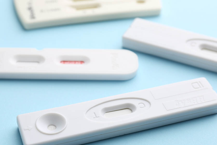 Several white plastic rapid test cassettes are arranged on a light blue surface, each with visible windows for result display.