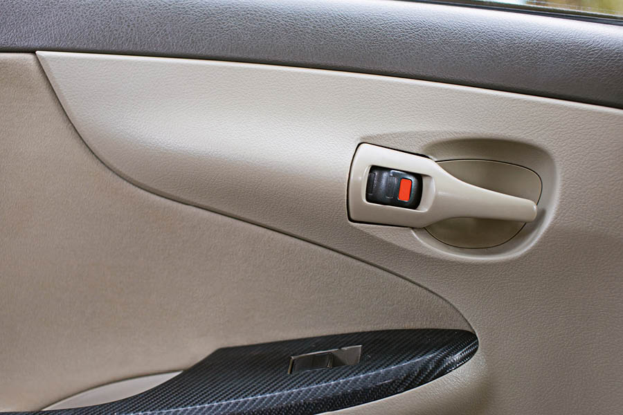 Close-up of a beige car door interior with a silver door handle, black lock switch showing red indicator, and a black armrest.