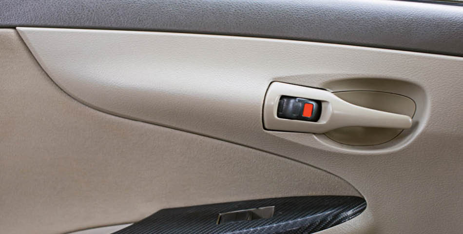 Close-up of a car's interior door panel showing the door handle, a lock switch with a red indicator, and part of the window control.