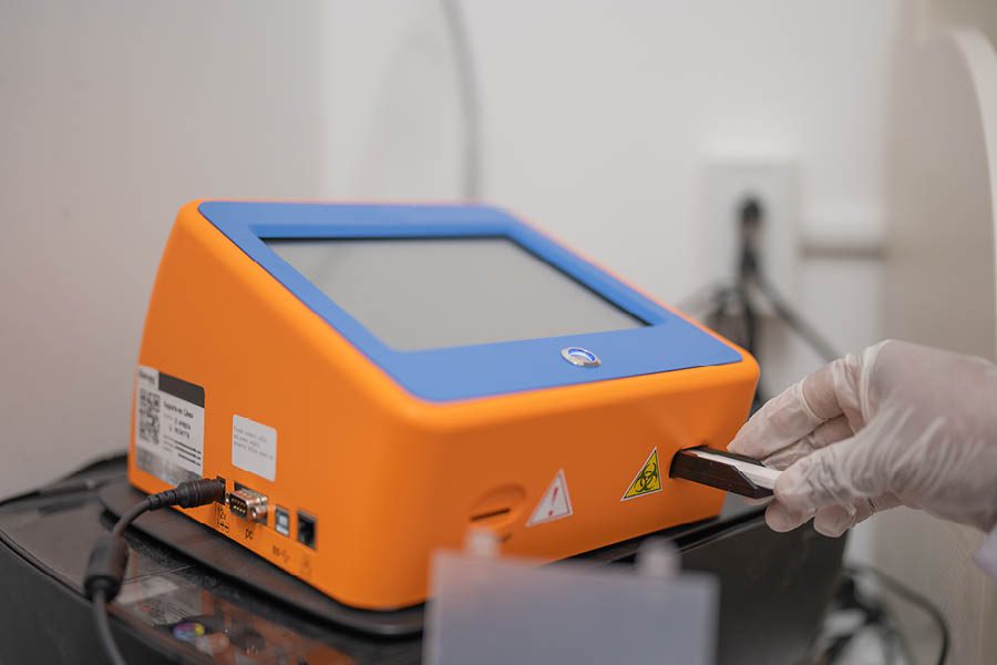 A gloved hand inserts a USB stick into an orange and blue electronic device with a touchscreen.