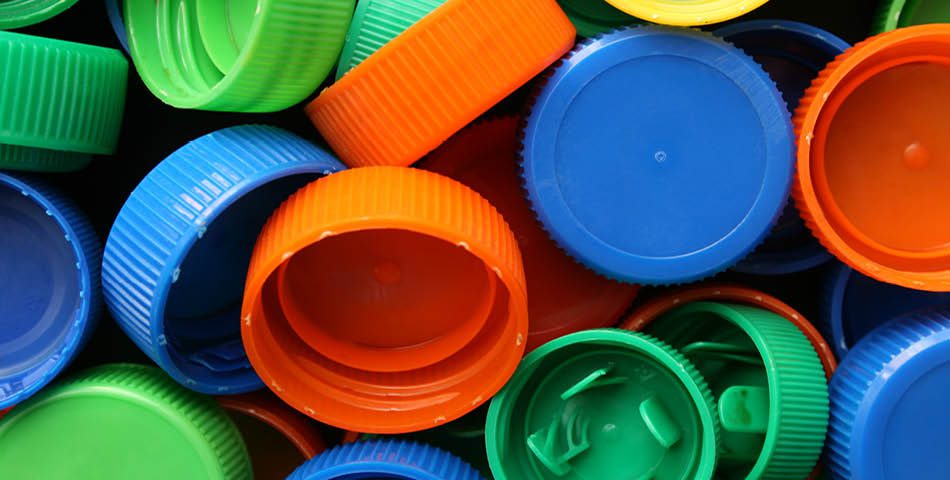 A pile of assorted plastic bottle caps in blue, orange, green, and yellow colors, made from chemical-resistant & recyclable thermoplastics like durable polyolefin compounds.